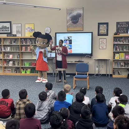Mya mascot reading to children in library or classroom setting